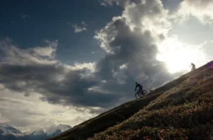 Two people are riding mountain bike up a paved hill.