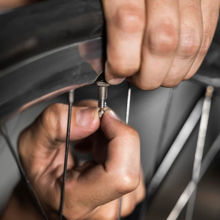 Hands using a tool to adjust or repair a bicycle spoke.