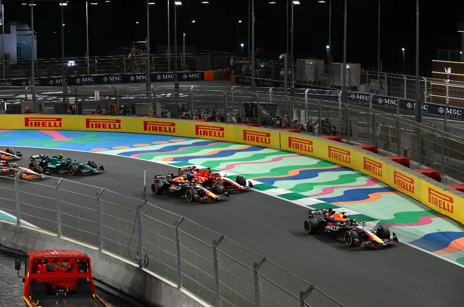 A group of Formula 1 cars racing around a brightly lit track at night