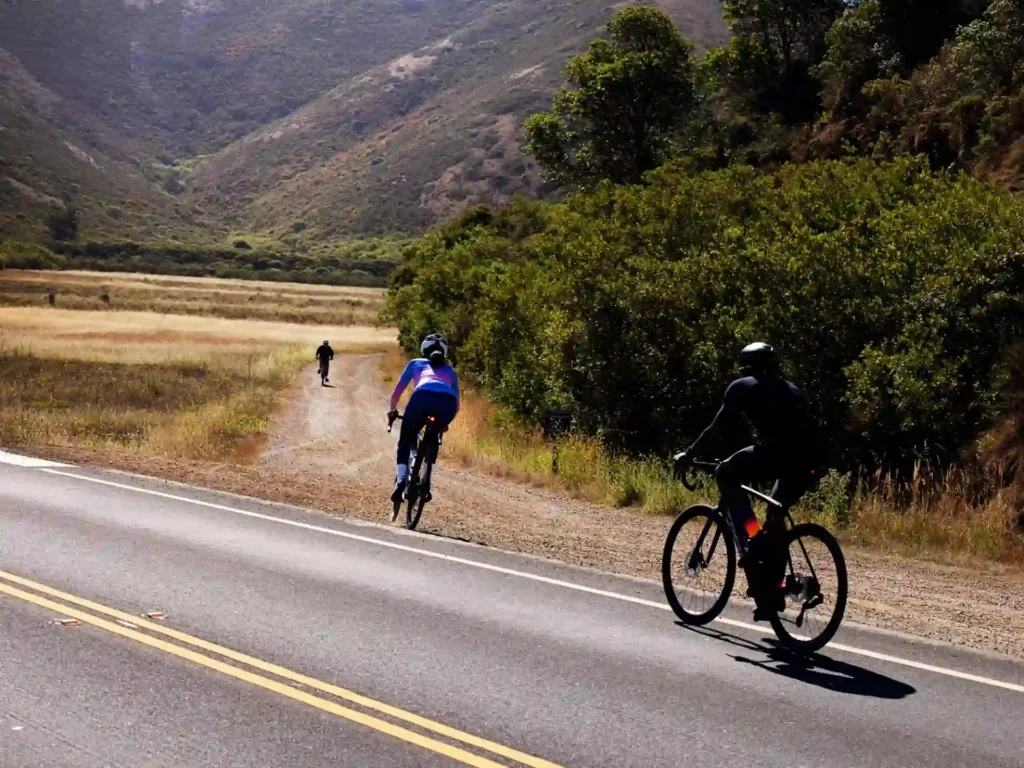 Cycling on a rural road with a paved surface and visible road markings surrounded by hills and vegetation.