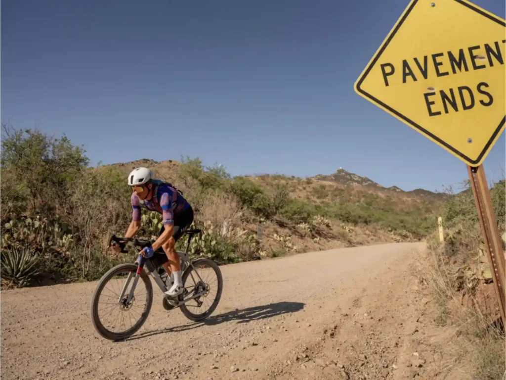 A cyclist on a gravel road, with a "Pavement Ends" sign in the background