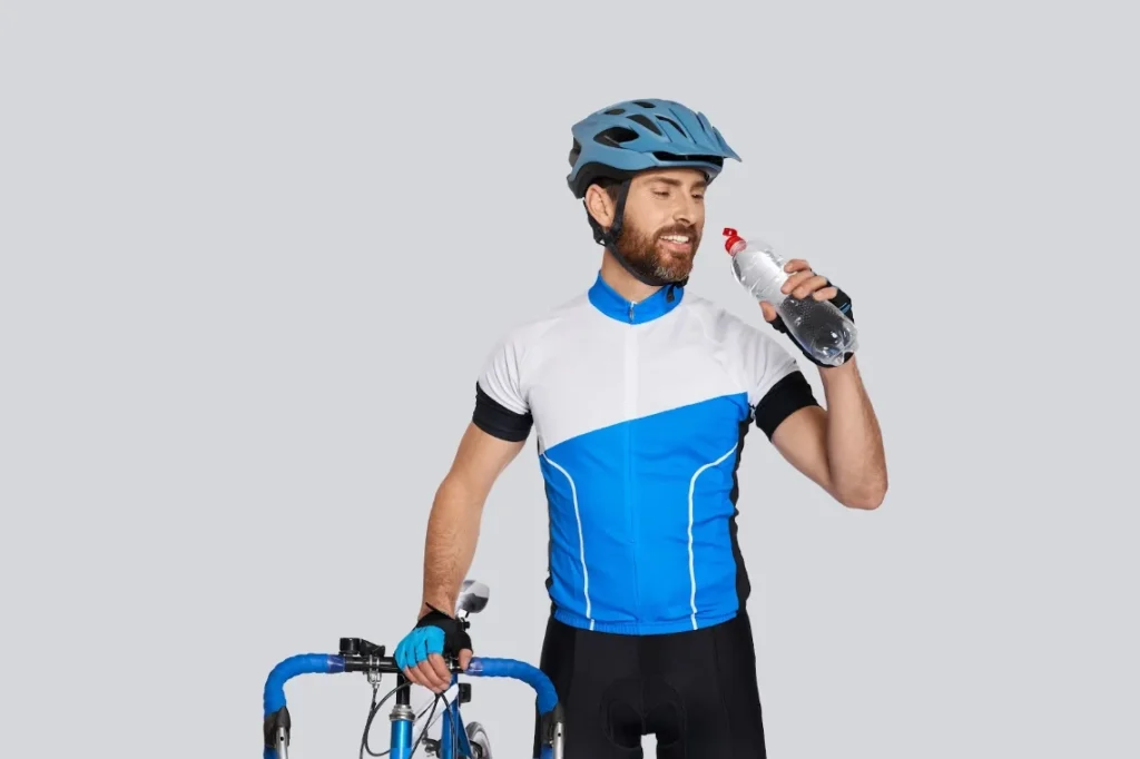 Cyclist wearing a blue and white jersey and helmet drinking water to stay hydrated during cycling