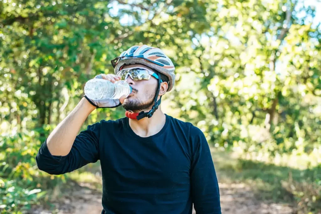 sportswear and helmet drinking water while cycling outdoors in nature