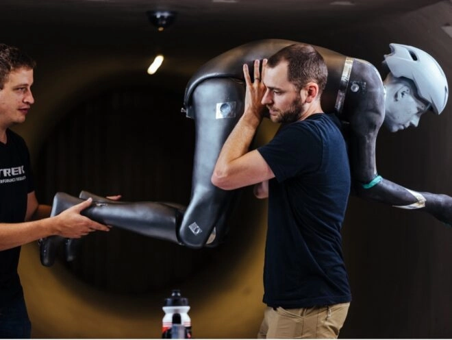Two technicians place the robot 'Manny' on a bike in a wind tunnel to simulate rider movements for aerodynamic testing.
