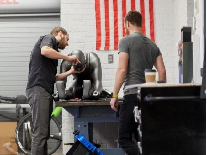 Two technicians assemble the robot 'Manny', preparing it for cycling tests and aerodynamic experiments.